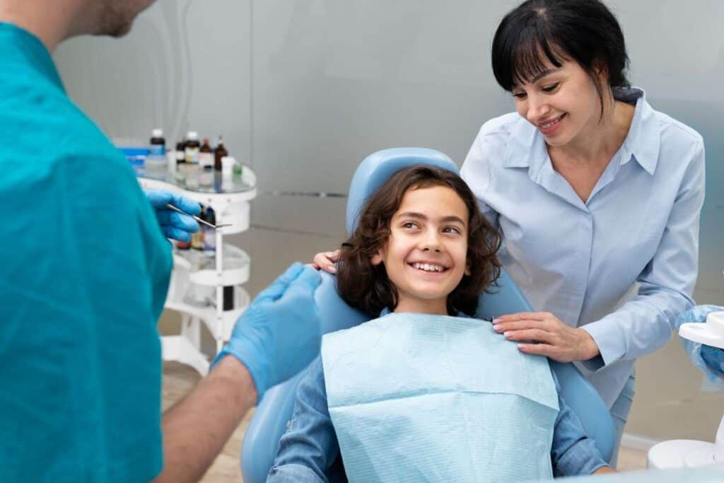 Bambina felice in poltrona odontoiatrica durante una visita dentistica con assistente e dentista.