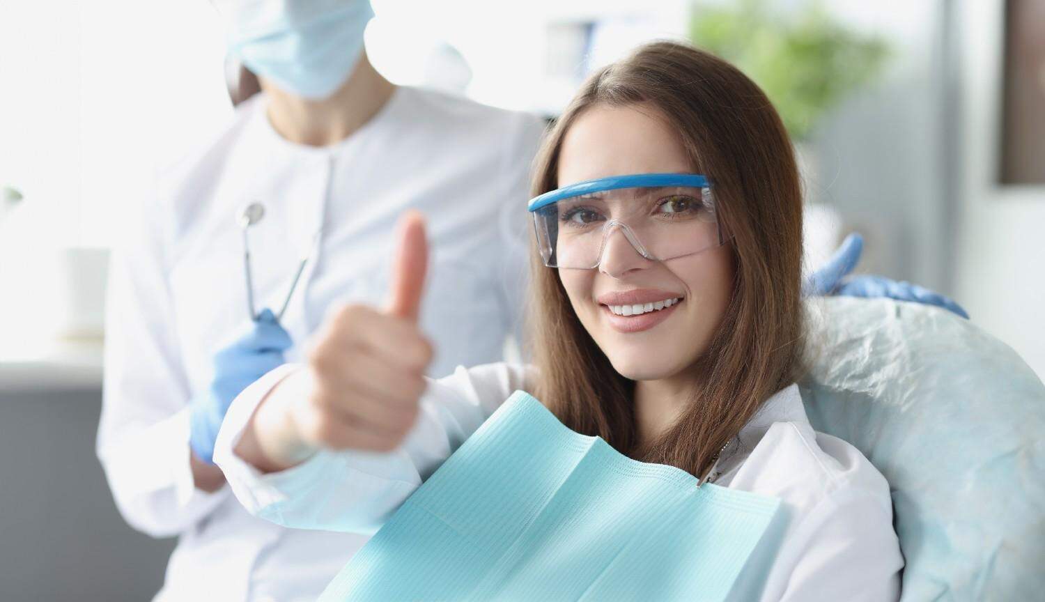 Paziente sorridente con protezione visiva e poltrona odontoiatrica, pronta per trattamento dentale i.