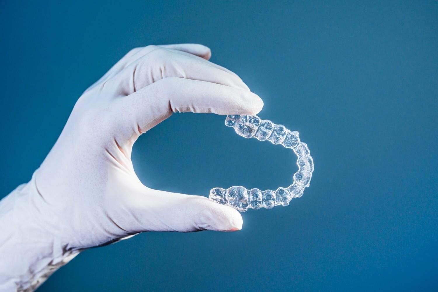 Transparent Invisalign aligner held by a gloved hand, ready to be applied to the teeth.