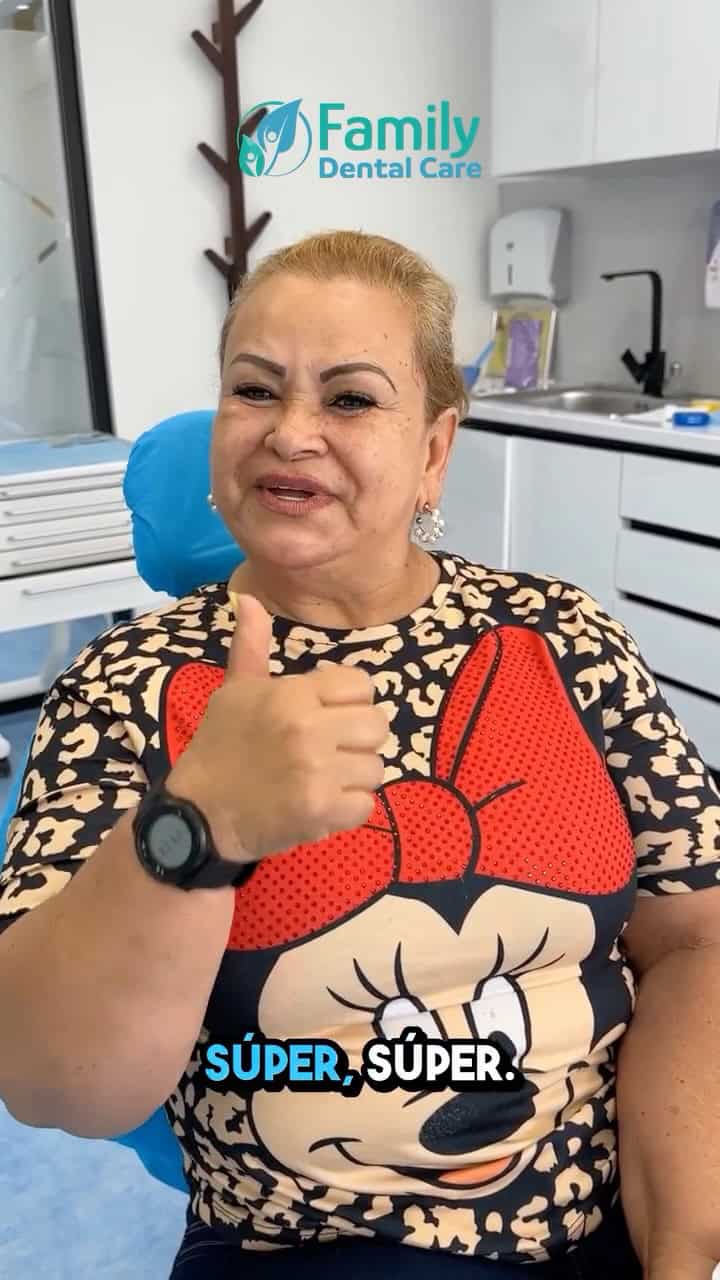 Un'anziana donna sorridente in clinica odontoiatrica, mostra un pollice in su, con il logo Family De.