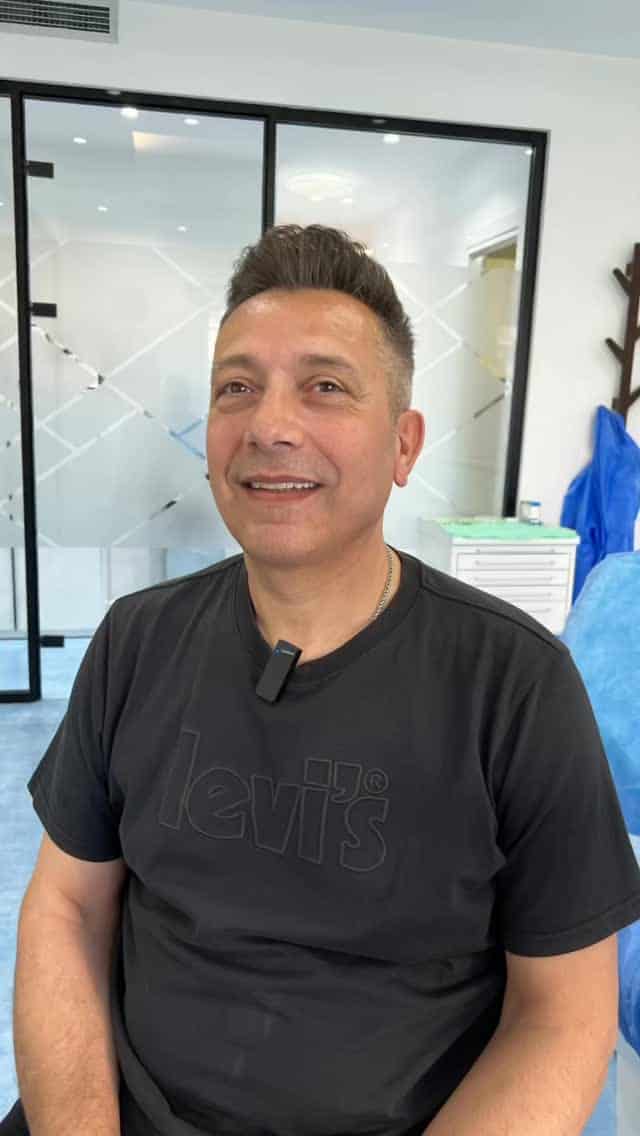 Dentista sorridente con camice nero in studio odontoiatrico moderno.