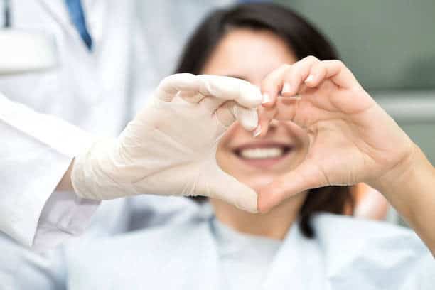 Dentista con paziente che forma un cuore con le mani in studio dentistico.