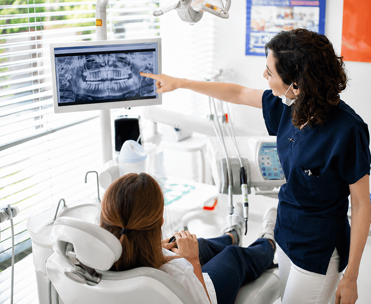 Dentista mostra radiografia dentale a paziente seduta in poltrona.