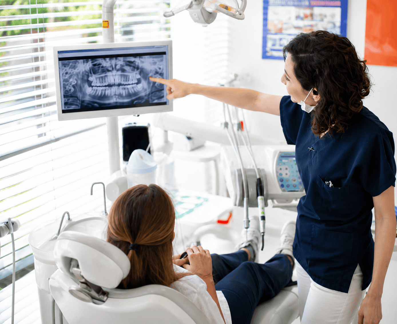 Dentista mostra radiografia dentale a paziente seduta in poltrona.
