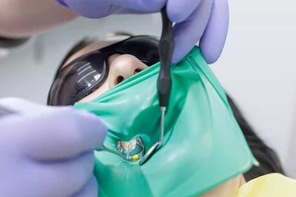 Trattamento odontoiatrico con mascherina e strumenti, paziente sotto anestesia locale.