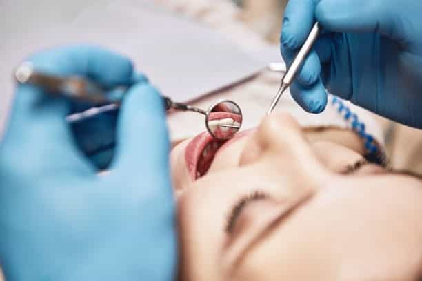 Paziente riceve un trattamento odontoiatrico, con strumenti e guanti blu, sotto la supervisione di u.