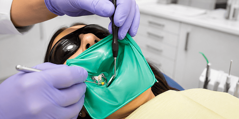 Un dentiste effectue un traitement endodontique sur un patient avec une protection oculaire et un masque facial.