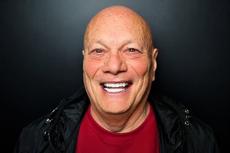 Uomo anziano con sorriso ampio e denti visibili.