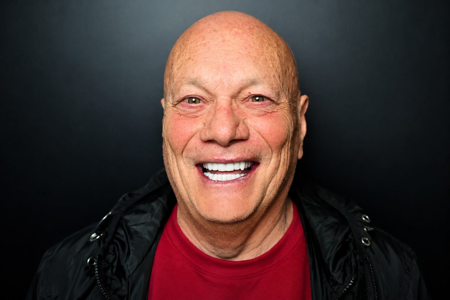 Uomo anziano con sorriso ampio e denti visibili.