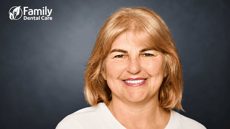 Donna sorridente con capelli biondi e sfondo scuro.